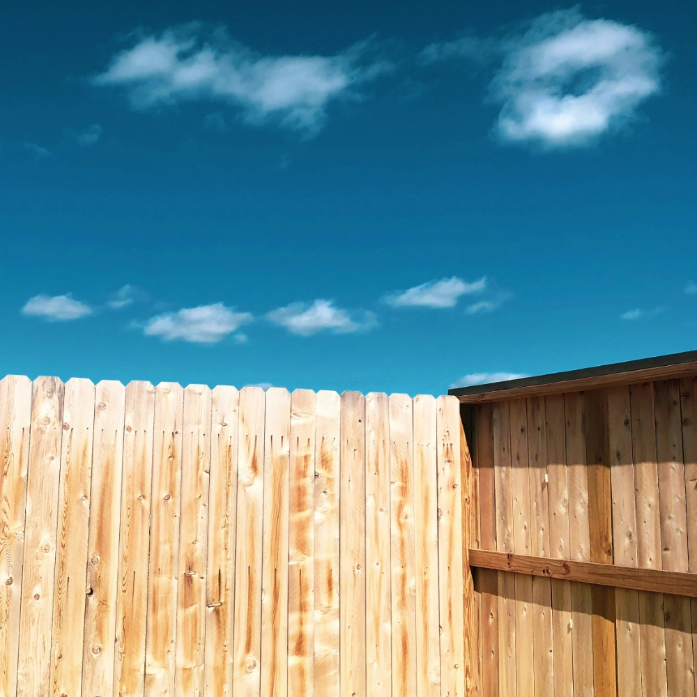 A clear blue sky with soft clouds over a wooden privacy fence with angled corners in miami valley oh