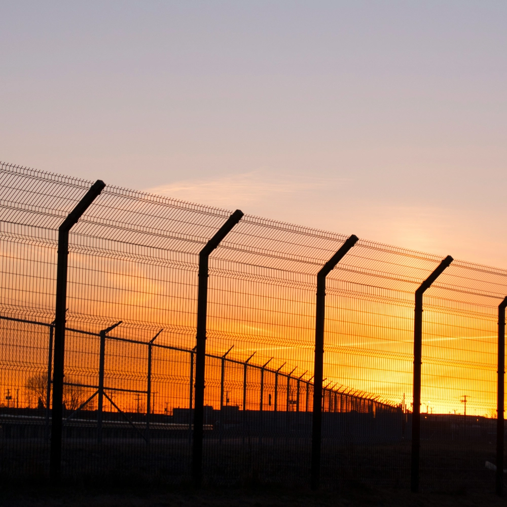 A metal security fence with angled barbed tops silhouetted against a bright orange sunset sky in miami valley oh