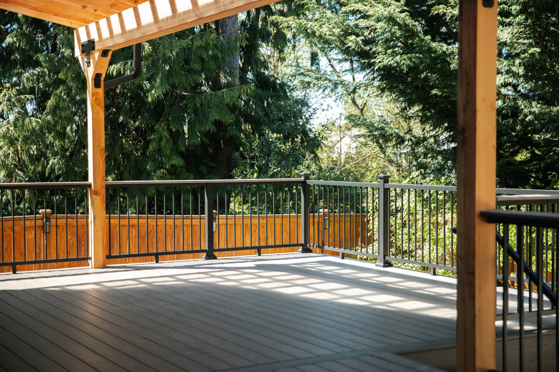 Covered wooden deck with pergola black metal railing and sunlight casting shadows surrounded by trees and natural forest backdrop in miami valley oh
