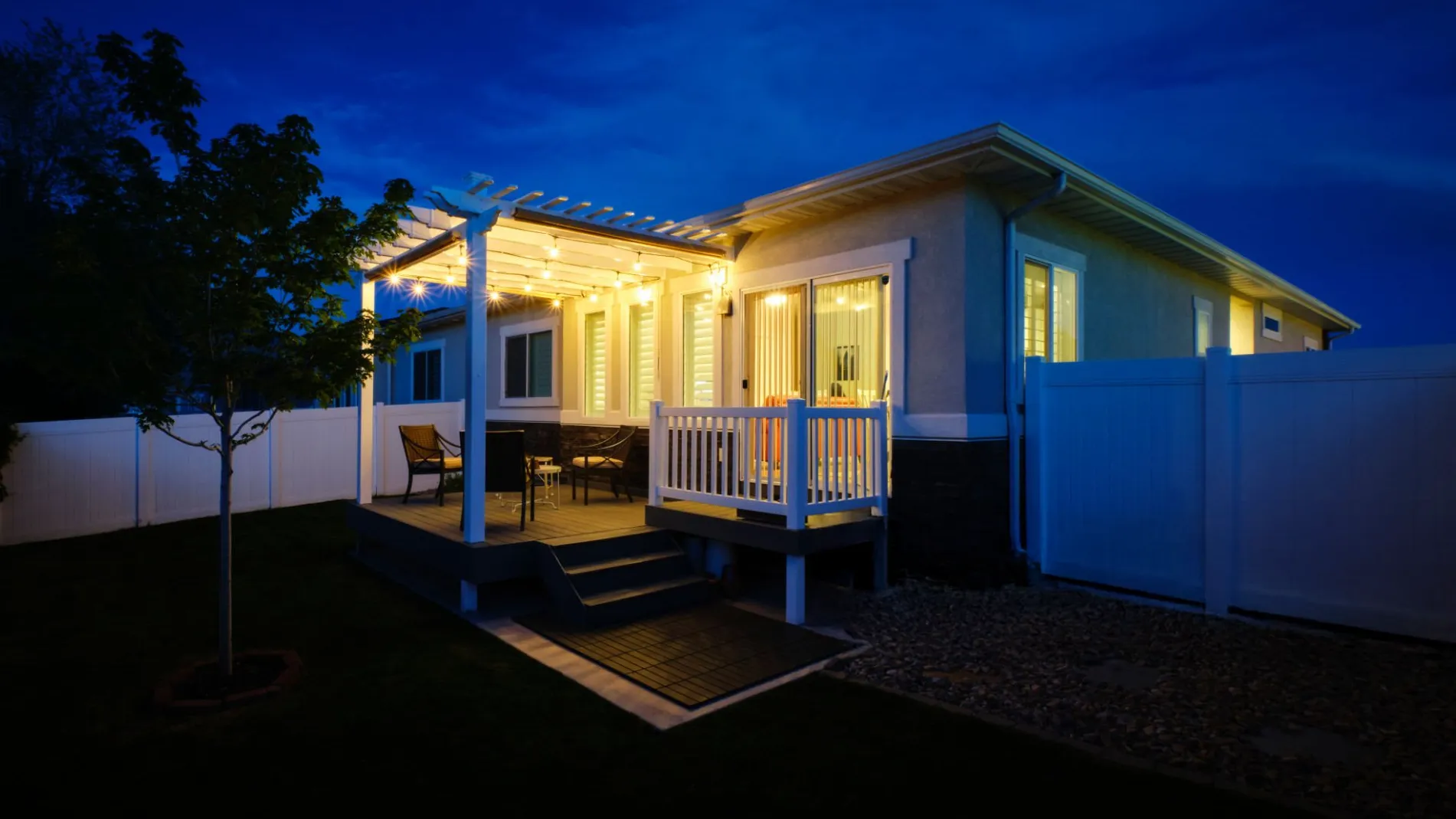 Modern house with pergola lighting on the custom residential deck with white railing and outdoor chairs and table with white fence in miami valley oh